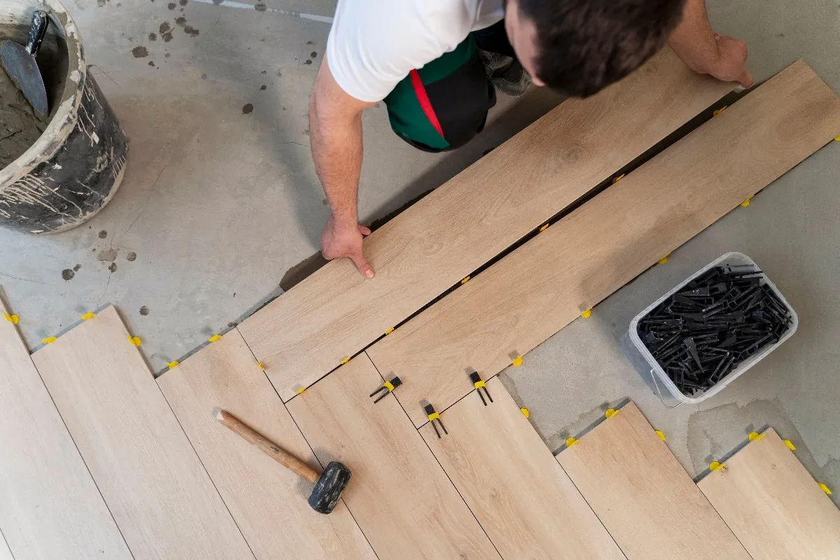 A man carefully installs wooden flooring, focused on creating a beautiful and sturdy surface for the room.