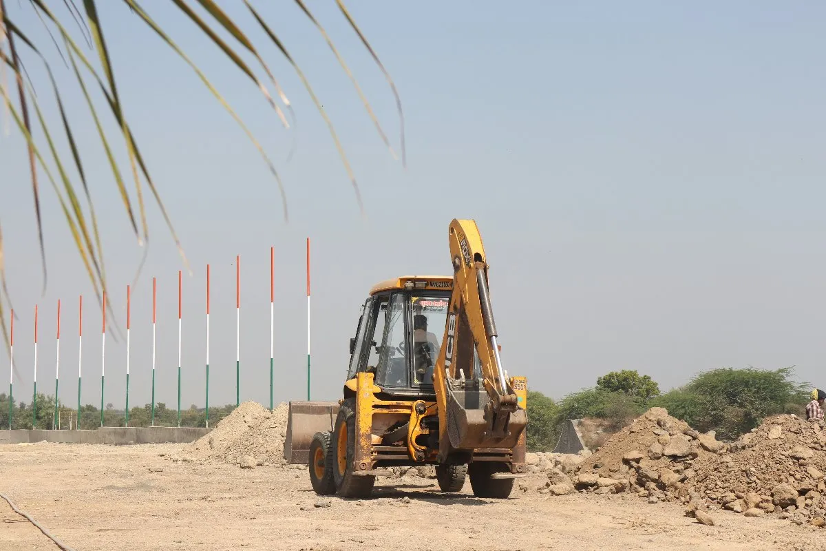 A backhoe rests on a dirt road, surrounded by earthy tones, ready for its next task in construction or landscaping.