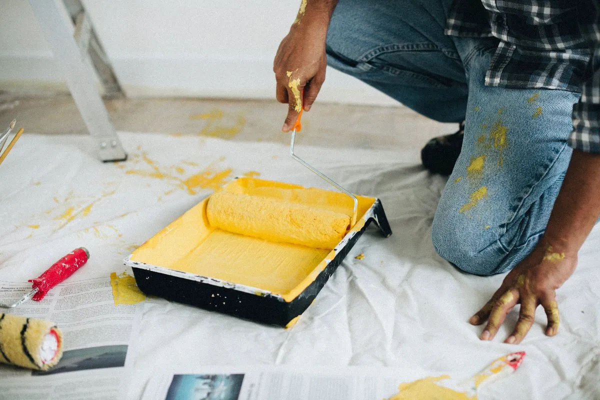 A man focused on painting a white floor with yellow paint, adding a cheerful touch to the space around him.