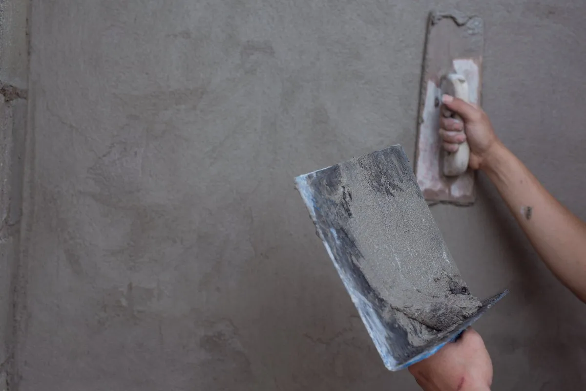 A person skillfully uses a trowel to spread cement smoothly onto a wall, focused on their task.